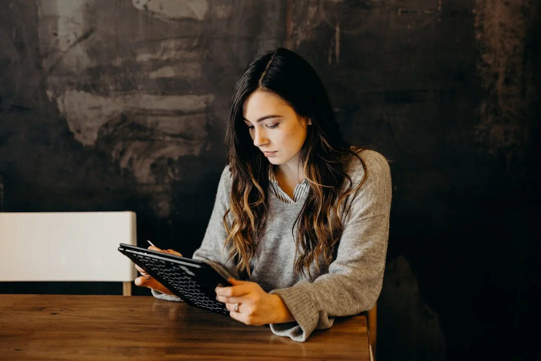 Hands using a tablet beside a laptop in a home office setting, showcasing online browsing.